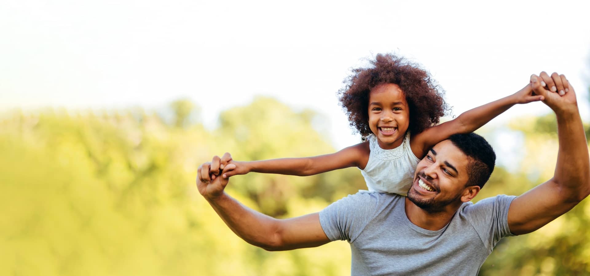 Black man with his daughter on his shoulders both smiling