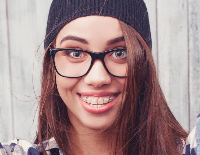 jeune femme brune à lunette souriante avec des broches