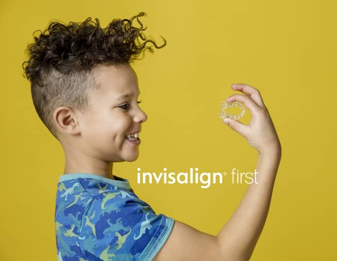 young boy looking at his hand holding invisalign aligner