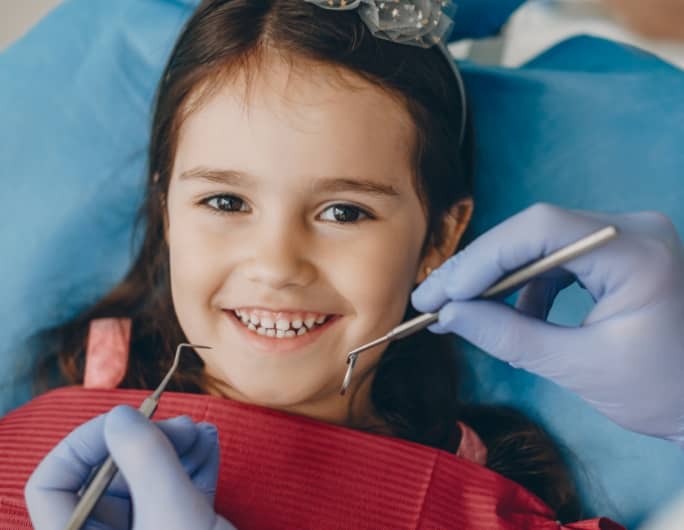 dentiste tenant des instruments entre ses mains avec jeune fille qui sourit à la caméra